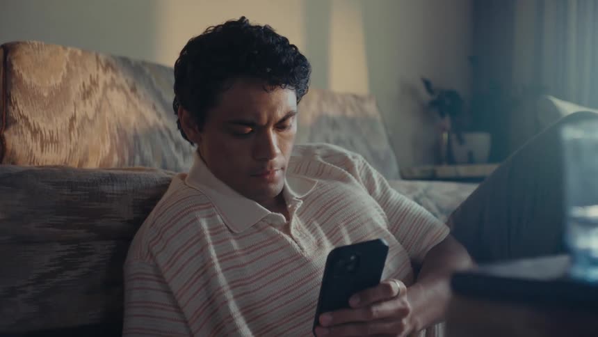 A man sits on his living room floor while staring at his smartphone