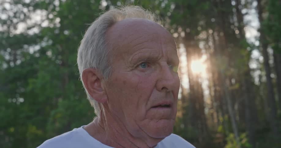 Close up of the face of an elderly man with the sun peeking thorugh trees in the background