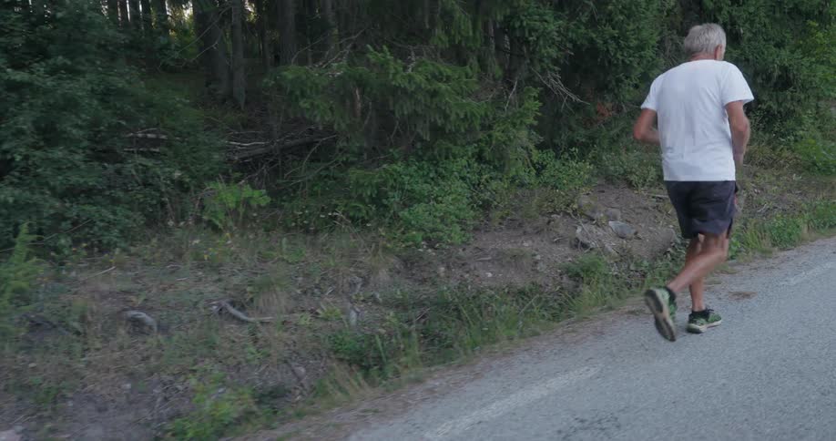 Slow motion of an elderly man running on a road in a forest