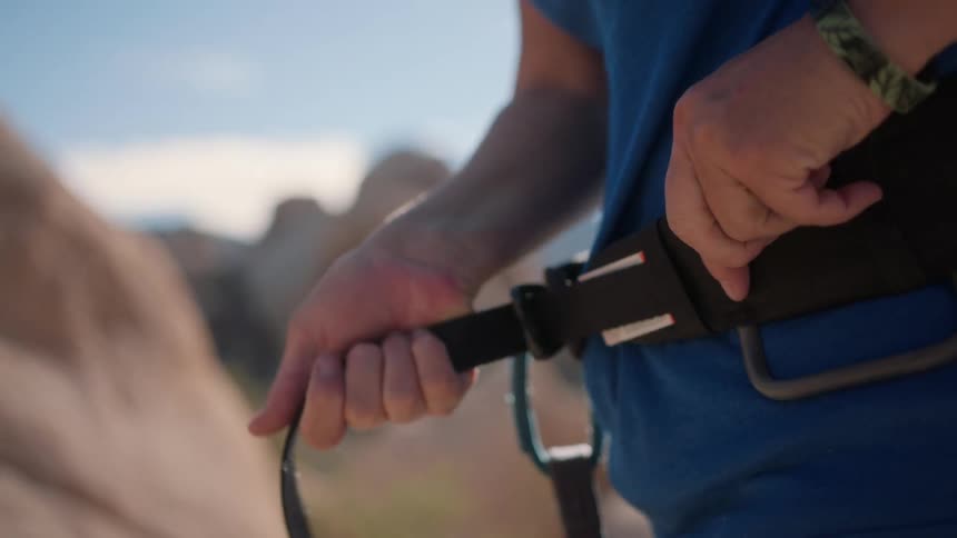 Close up of a person tying and strapping a belt around their waist outdoors preparing for a hike