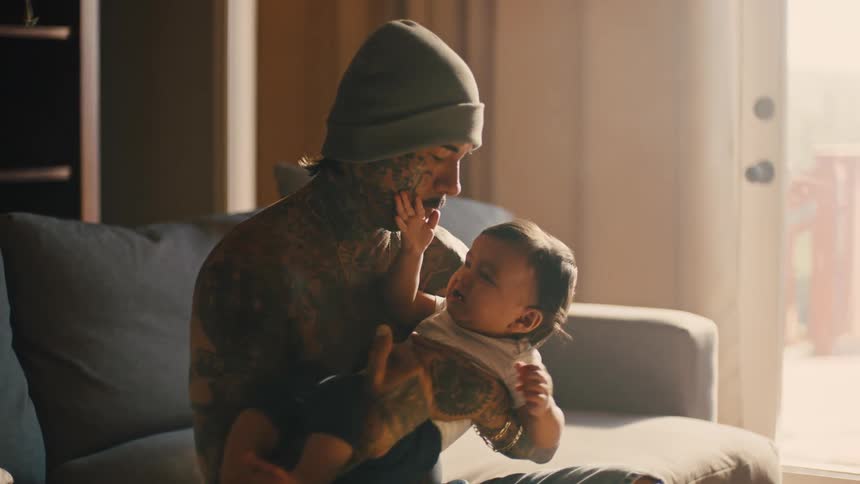 A man sits on a couch holding a baby in his arms while the baby cries