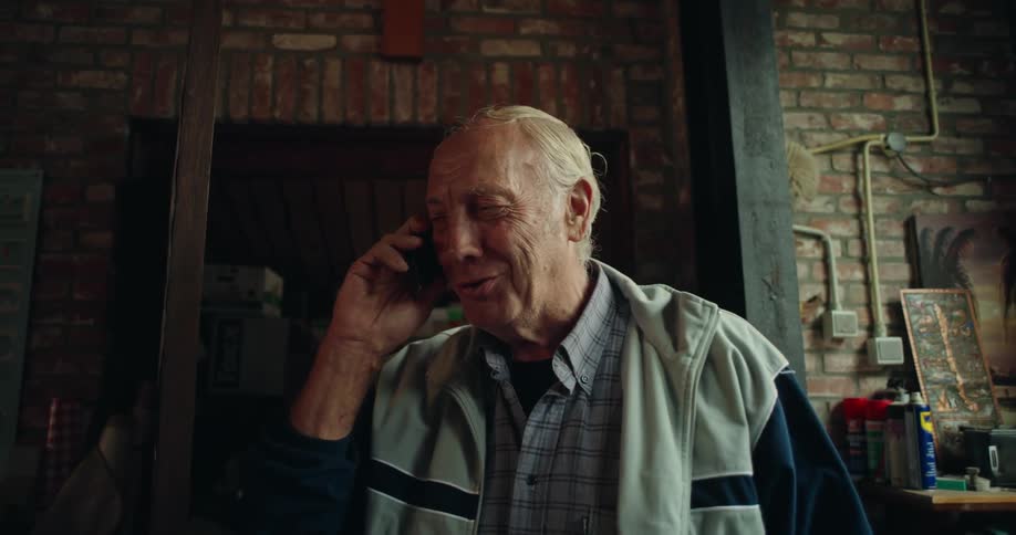 An elderly man is talking to someone on the phone that is in his ear and he is happy