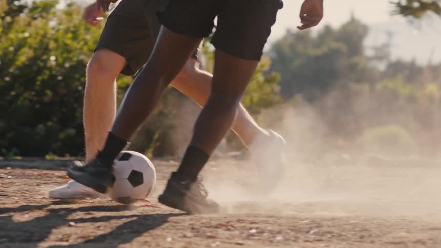 Two young men are playing soccer outdoors on a windy summer day