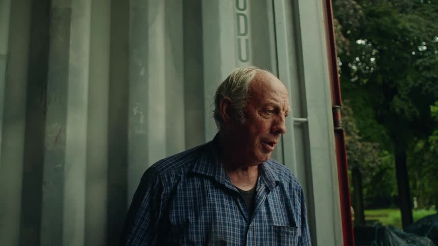 An elderly man inside a shipping container speaking to someone