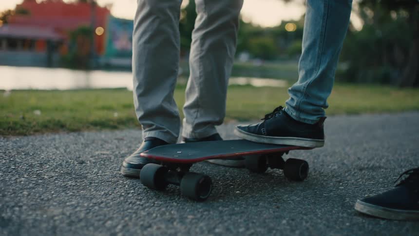 The legs of two people and one of them is putting his foot on top of a skateboard