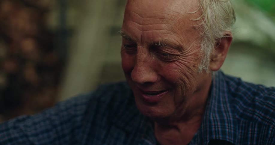 Close up of an older mans face looking forward pouring a drink