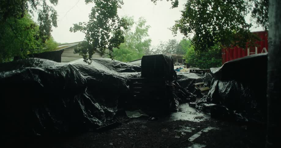 Black tarpaulin covering debris in an outdoor area with trees in the background