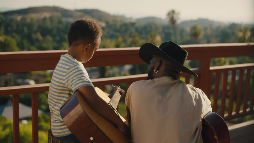 Man in hat next to boy holding guitar