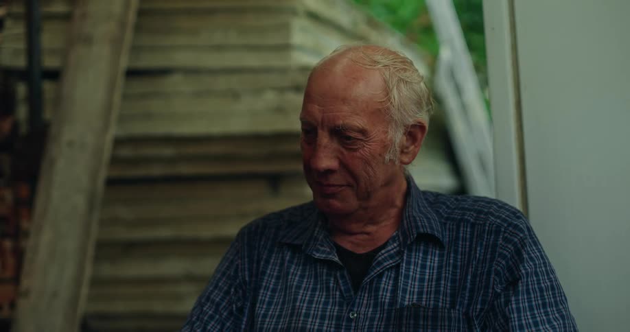 An elderly man sitting outside looking toward the ground contemplatively