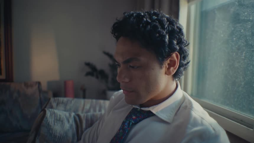 Man in white shirt and tie sitting on a couch looking to the side