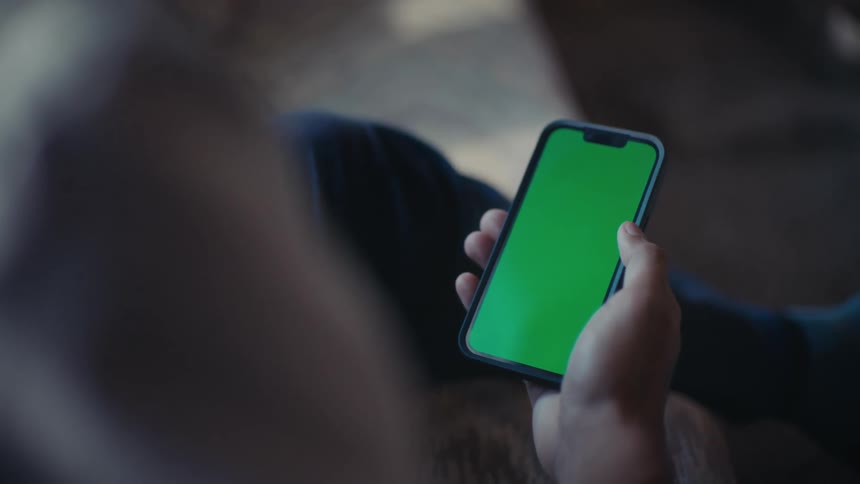 A person holds a smartphone with a green screen in an indoor setting