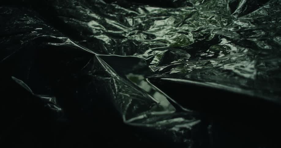 A closeup of a crinkled black plastic surface small pools of water over it