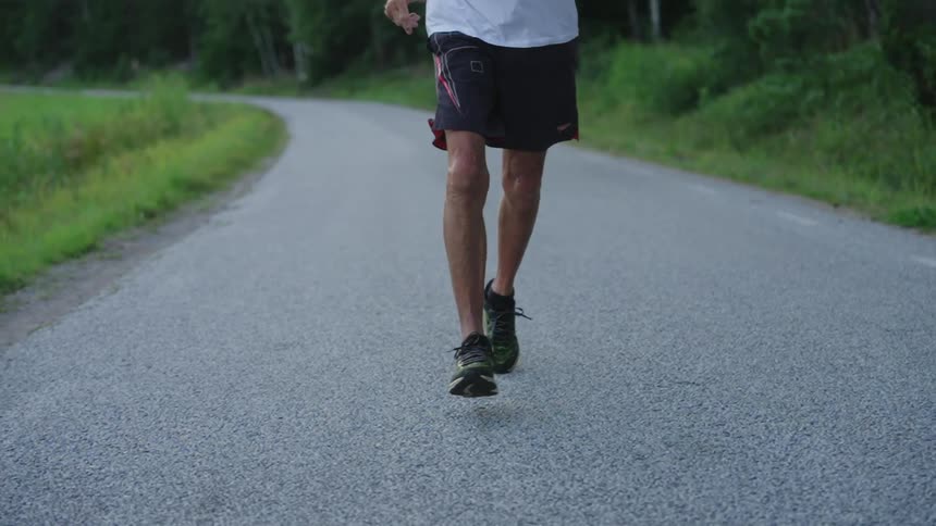 A man shown from waist to feet is running down a street in slow motion