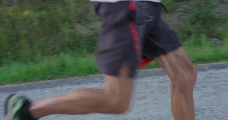 An older man running in sneakers on a roadway in the middle of the day with green grass and trees on either side of the road