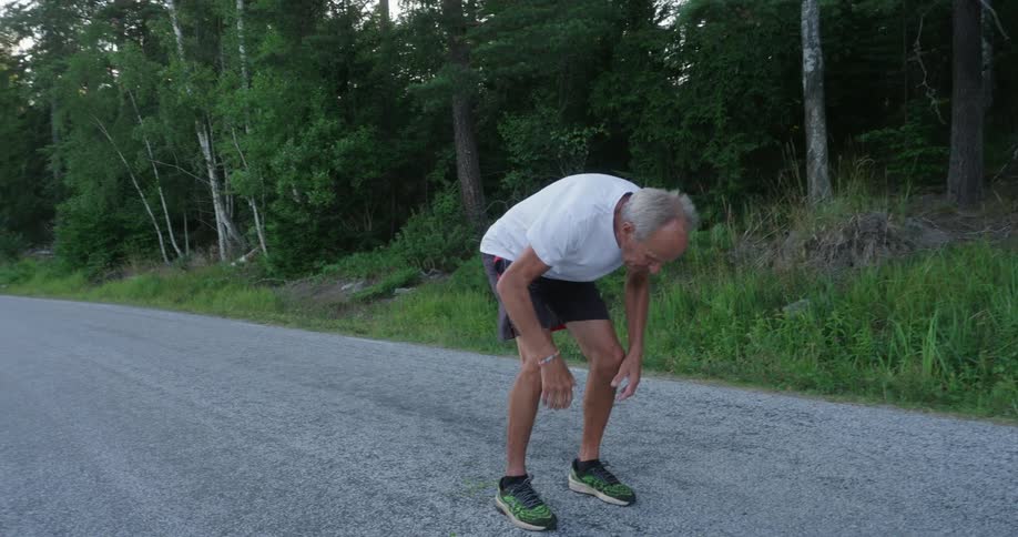Elderly man running and stopping putting his hands on his knee