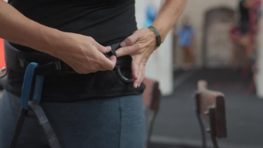 A closeup of a persons midsection as they fasten a blue climbing harness around their waist
