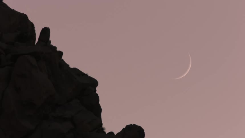 Silhouette of a mountain against the purple sky and the waning moon visible