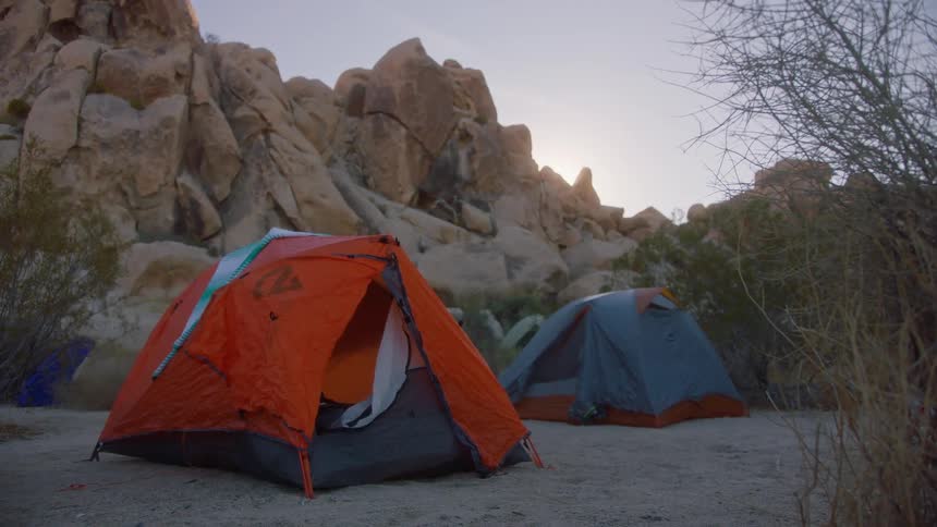 A blue and red tent set up at the base of rocks in nature