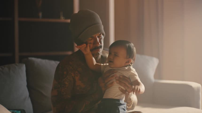 A father holding his infant daughter on his lap as she cries sitting on his lap