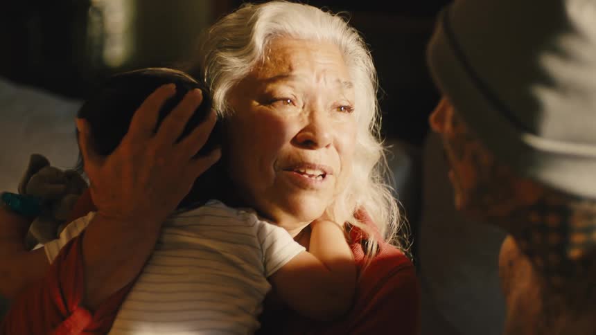 A grandmother holding a baby smiles and talks to her tattooed son