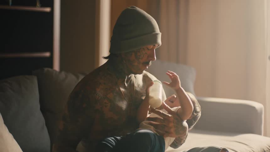 Father giving a bottle to his little son on his lap
