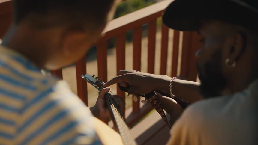 A man in a cowboy hat is teaching a little boy next to him about the strings of a guitar