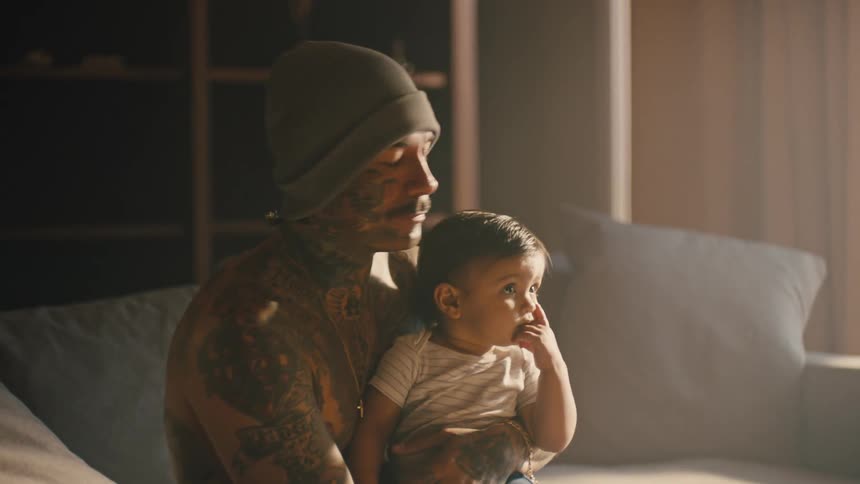 A father holds his toddler son on his lap while sitting on the couch