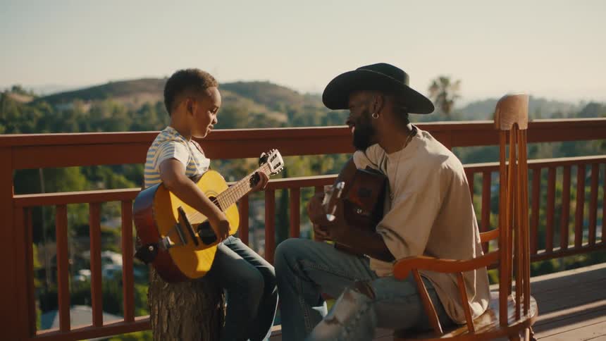 A father teaches his son to play guitar outdoors on a sunny day