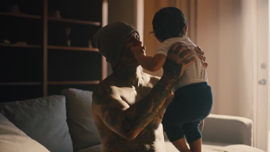 Father sitting in a shadowed living room lifts and holds his child