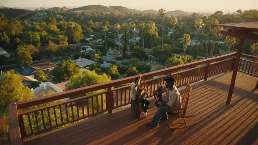 Boy sitting next to a man both with a guitar on the balcony of a building