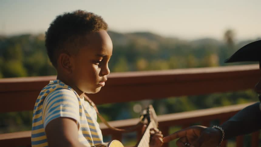 Little boy playing guitar and an adult next to him helping