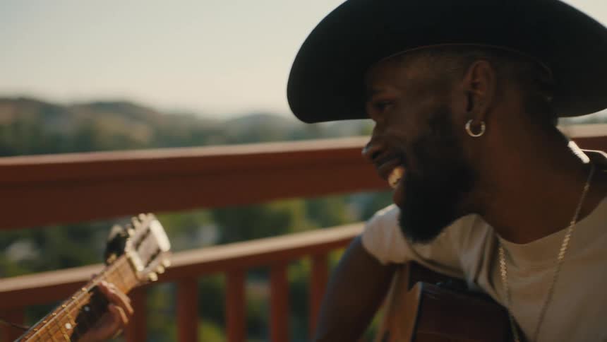 A father teaches his son to play guitar outdoors on a sunny day