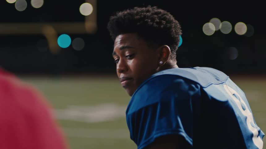 Person with an emotional expression wearing an american football uniform sitting and talking to a person next to him