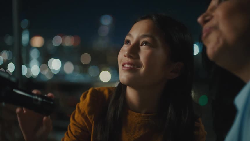 Mother and daughter talk smile and look at the sky at night while the daughter is holding a telescope