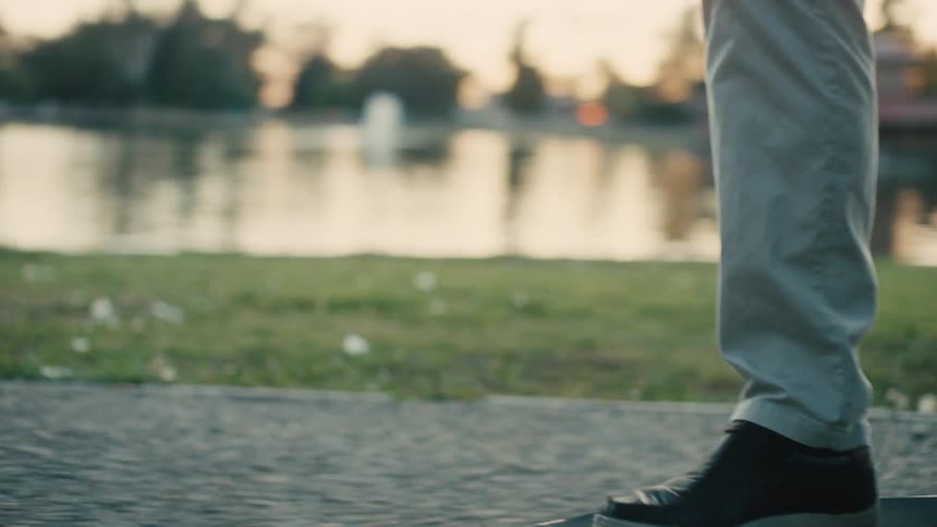 One person skateboards on a lakeside path while another person walks behind