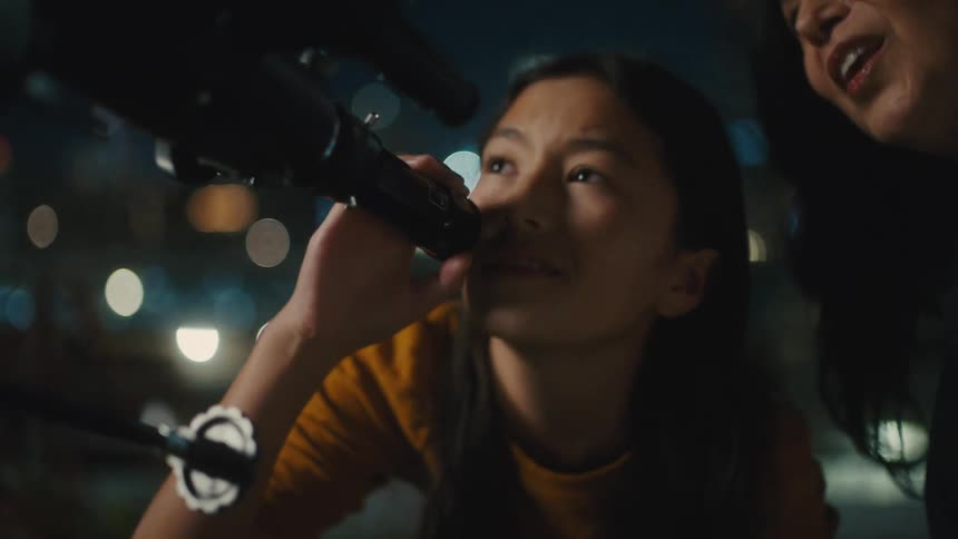 Woman next to a young girl looking into a telescope