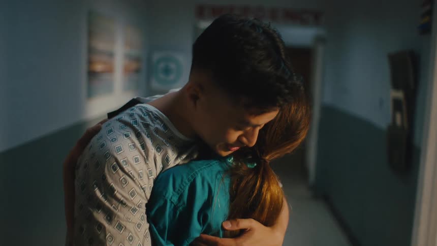 Patient in scrubs hugging a woman in a hospital hallway