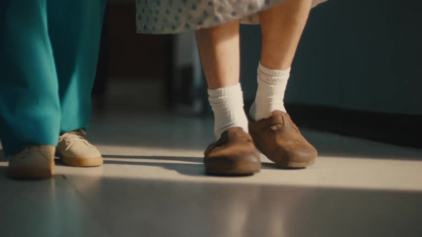 The feet of a patient in a medical facility walking next to a healthcare worker