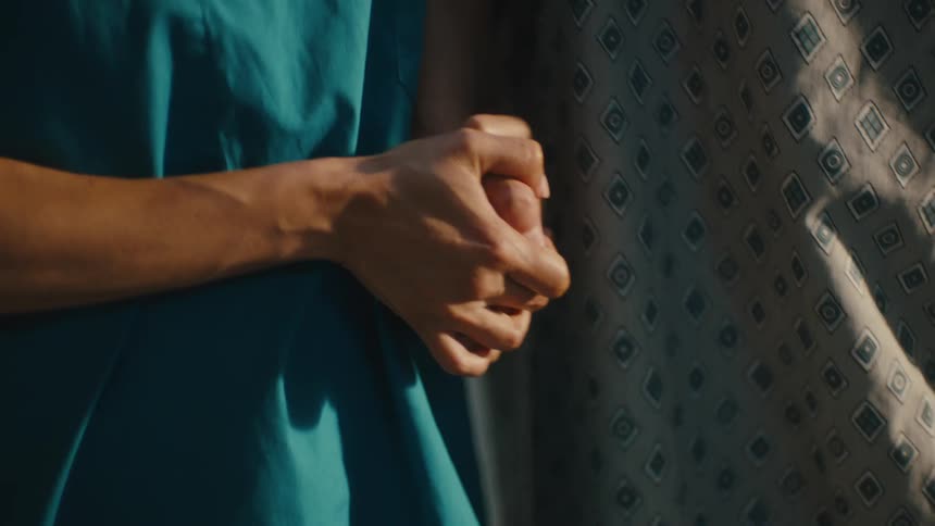 Close up of a patient in a gown holding hands with a nurse as they walk down a hallway and the nurse is smiling