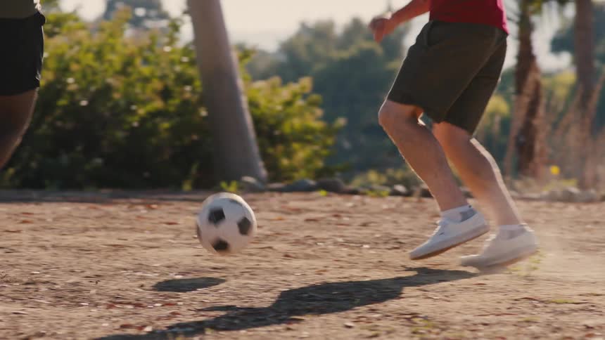 Two men playing soccer in a dirt field