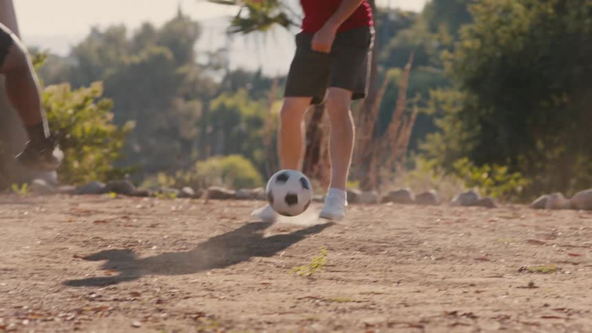 Two youths play with a soccer ball in a dusty field on a summer day