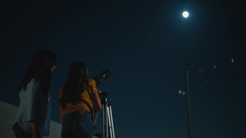 A mother and daughter looking through a telescope at night looking up at the moon