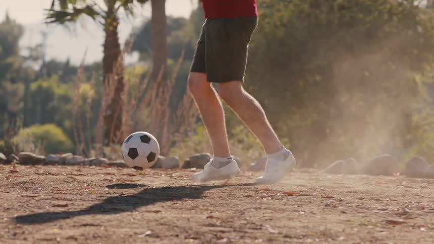 Two individuals are playing soccer on a dirt surface kicking up dust clouds