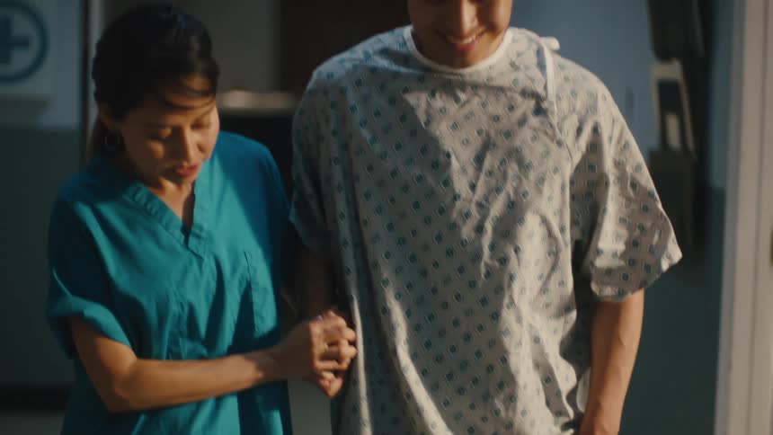 A nurse is helping an injured patient walk in a hospital hallway