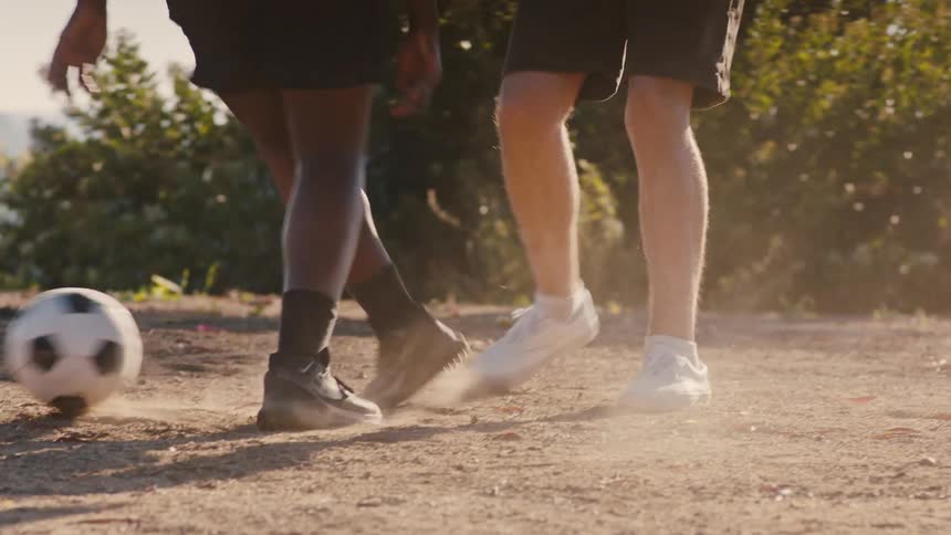 Two individuals are playing soccer on a dirt field kicking up dust