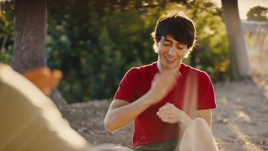 A young man in a red shirt using sign language to communicate with the person in front of him