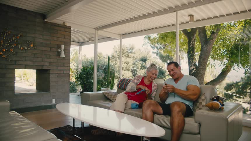 Mother and son seated on a couch in a modern porch enjoying knitting together