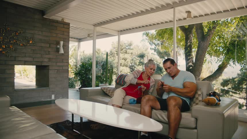 Elderly woman sitting in living room helping man next to her knit