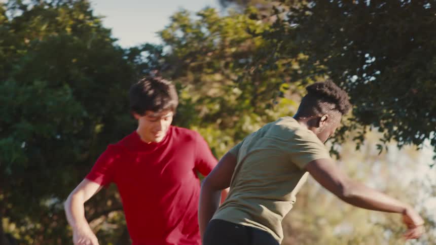 Two men kicking around a soccer ball on a gravel area outdoors in the sunlight