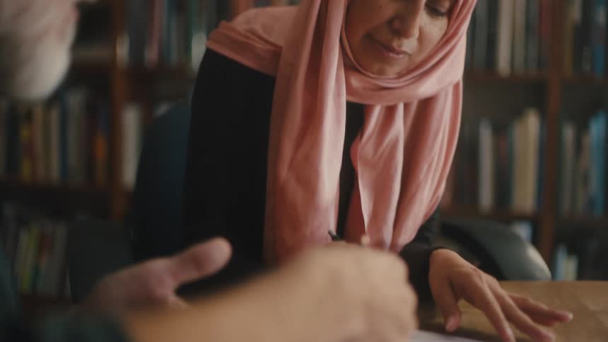 A bearded man explains details of a document to a woman wearing a pink headscarf